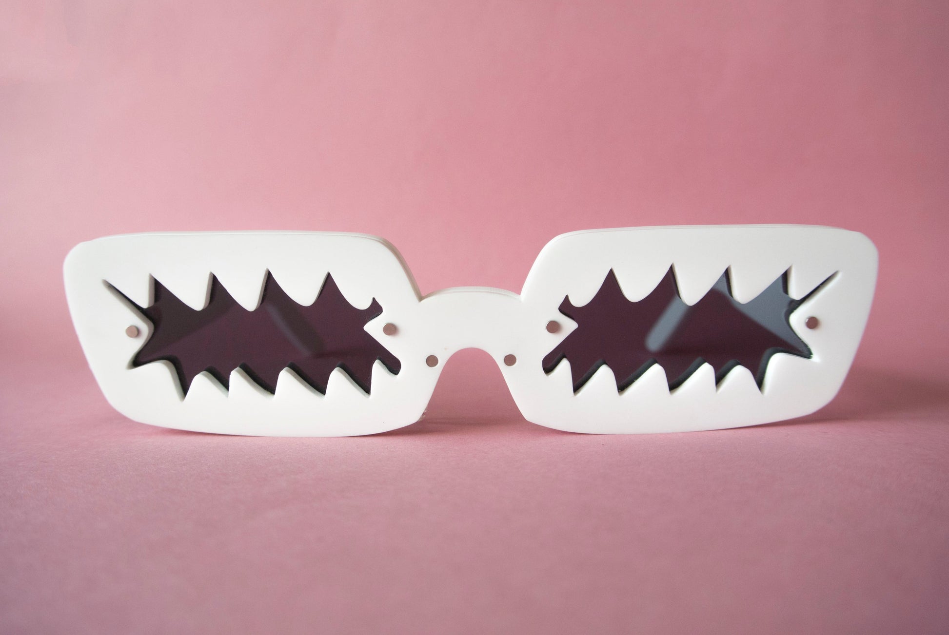 white glasses with black zigzag shaped lenses on a pink background 